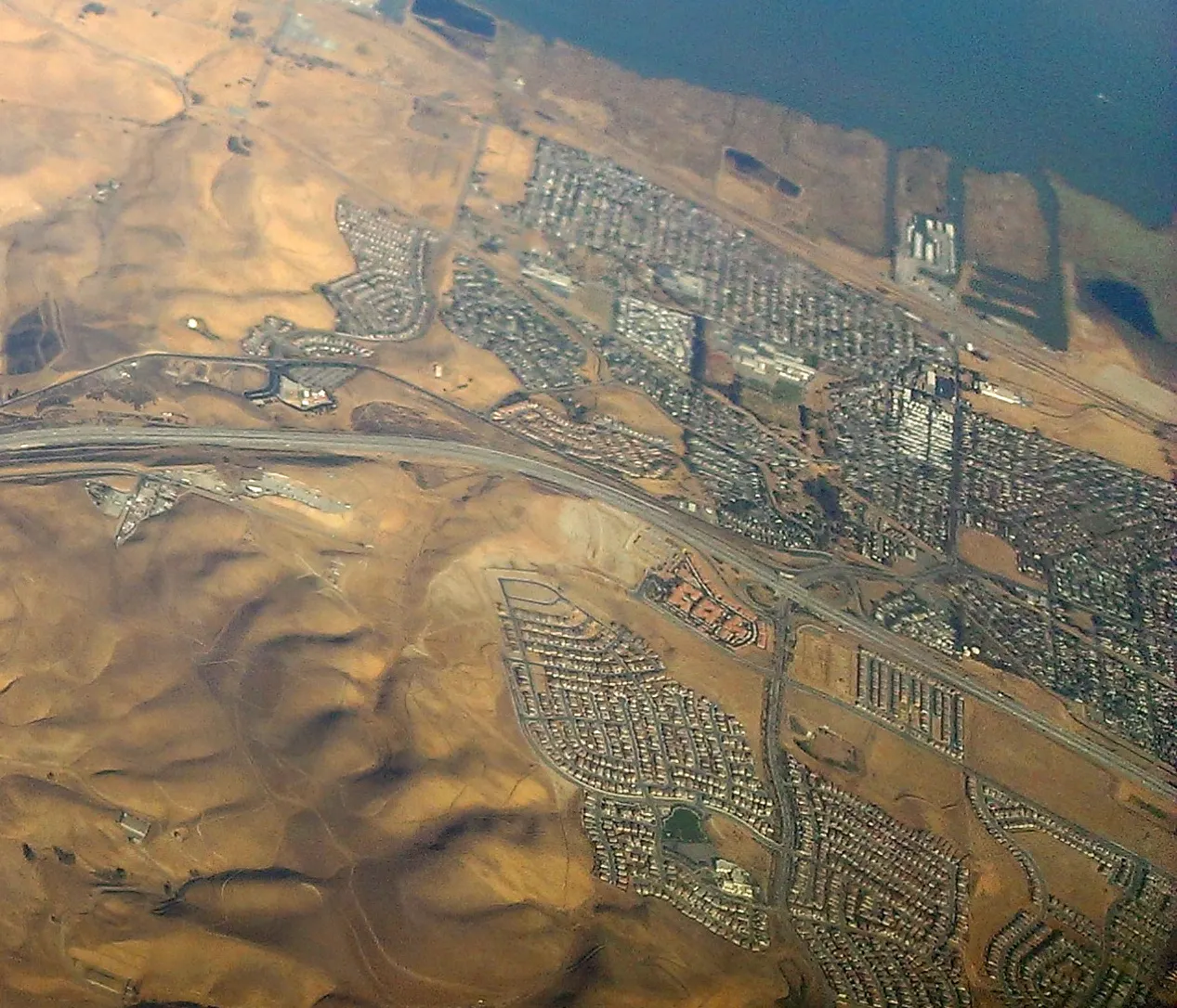 An aerial view northwest over Bay Point neighborhoods and industrial land beside Suisun Bay.