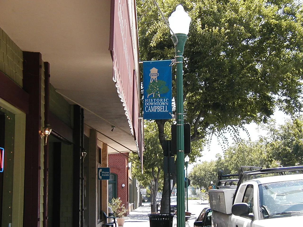Shopfronts, a downtown banner and trees along a sidewalk in downtown Campbell.