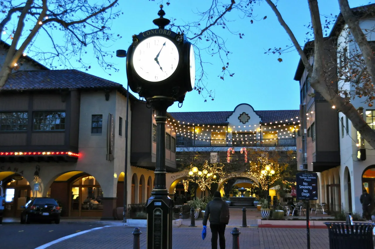 The Concord street clock and illuminated storefronts beside Todos Santos Plaza at dusk.