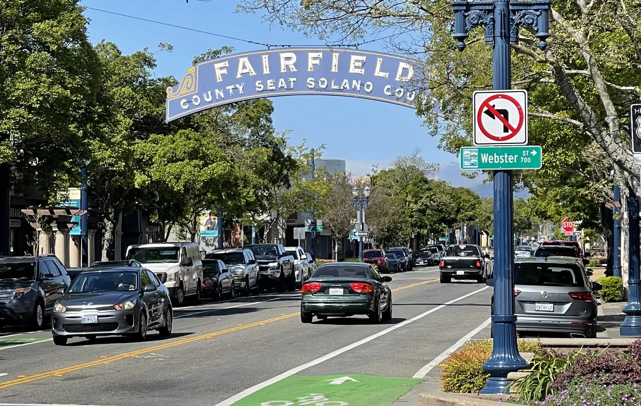 The Fairfield arch above a downtown street lined with trees, shops, and parked cars.