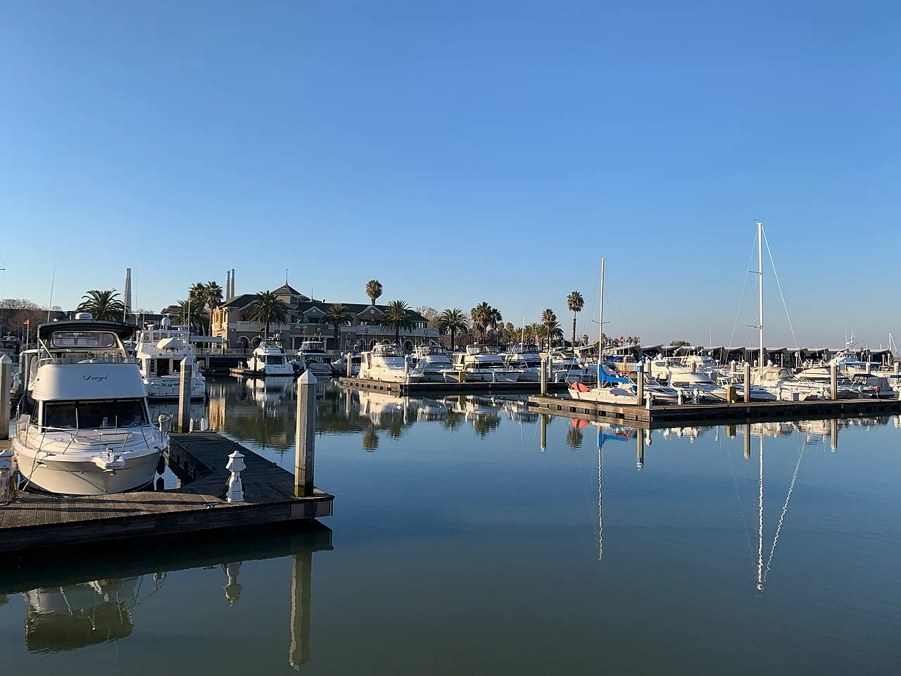 Boats and their reflections at Pittsburg Marina beside waterfront buildings.