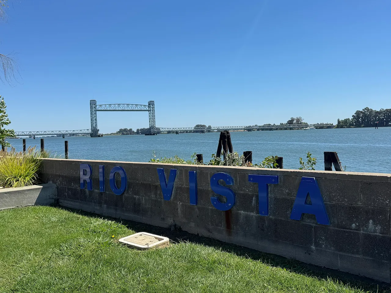A Rio Vista waterfront sign beside the Sacramento River, with the Rio Vista Bridge in the distance.