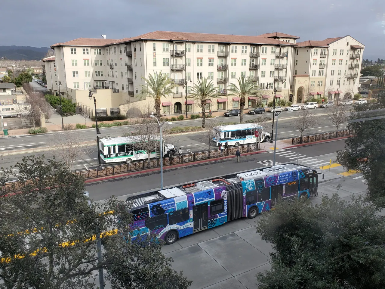Tempo and San Leandro LINKS buses beside San Leandro BART station, with apartments behind them.