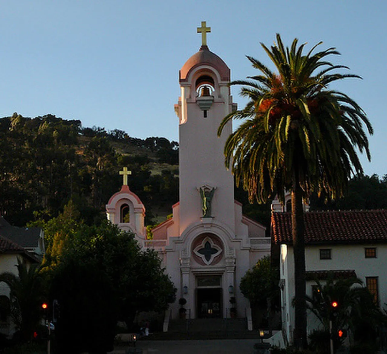 Mission San Rafael Arcangel and its bell tower, framed by a palm tree and wooded hills.