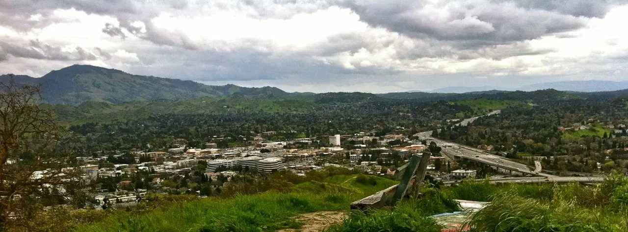 Walnut Creek neighborhoods and highways beneath green hills and a cloud-filled sky.